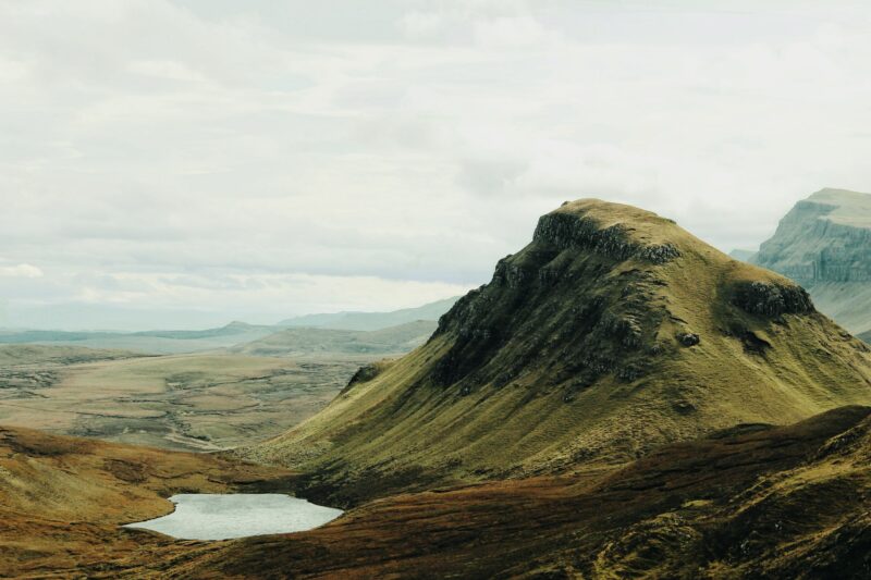 Lush green hills and a small lake under a cloudy sky, showcasing a serene landscape.