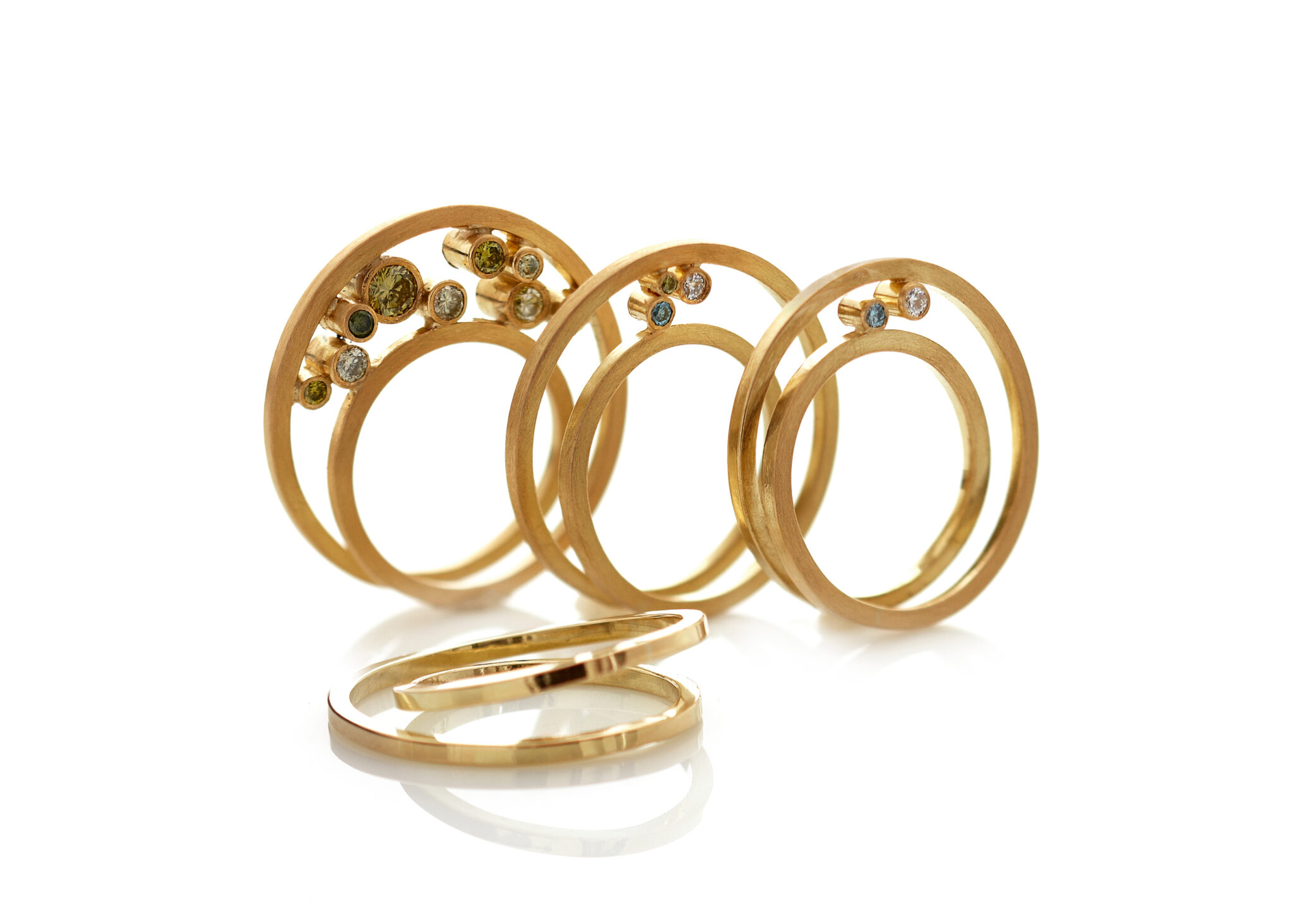 Three abstract gold rings with gemstones, showcasing a sculptural design, against a white background.