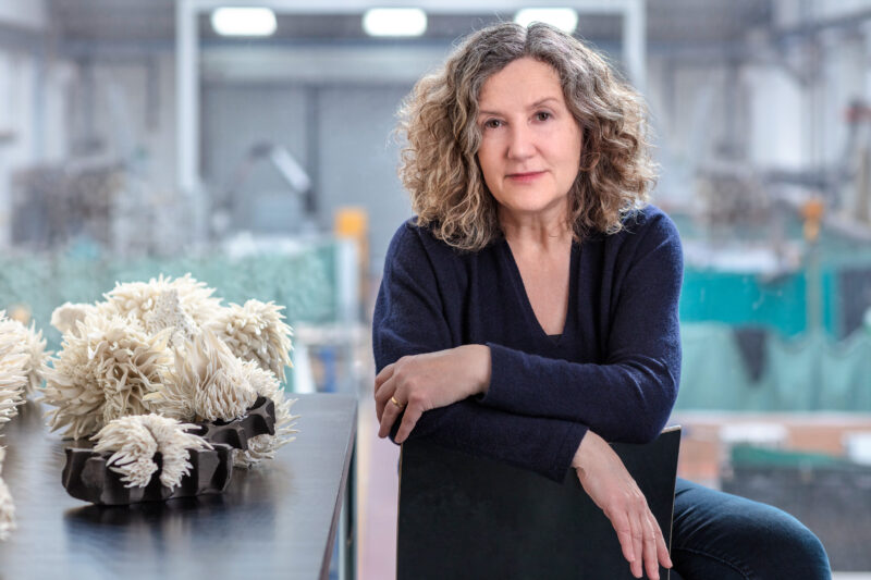 Portrait of Nuala O'Donovan seated at a table with artistic sculptures in a studio setting.