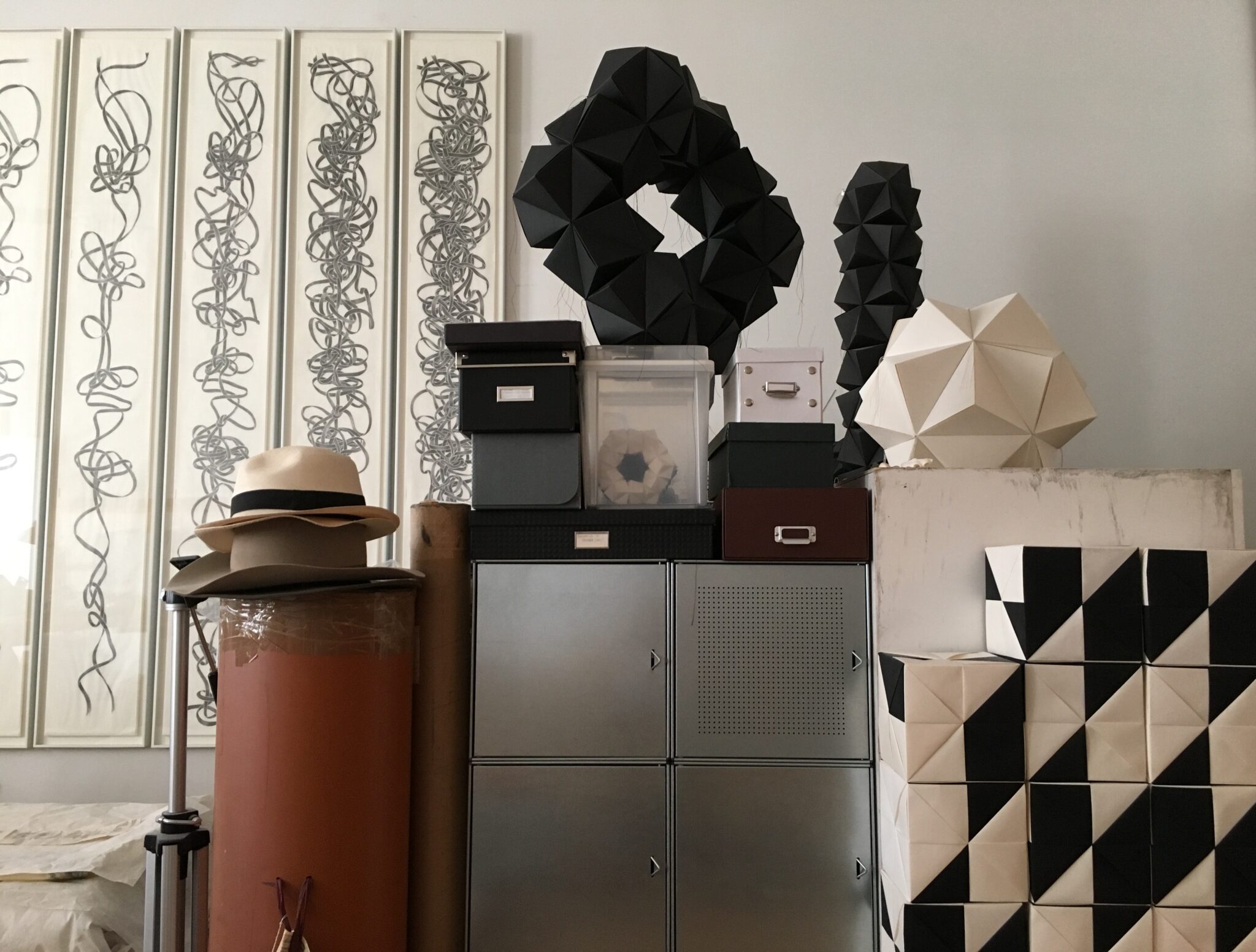 Modular sculptures and knot drawings in a studio setting, featuring geometric shapes and storage boxes.
