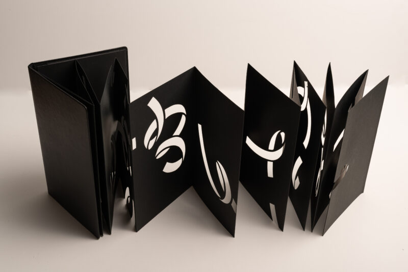 Hand-cut black leporello with white cut-out letters, displayed open against a light background.