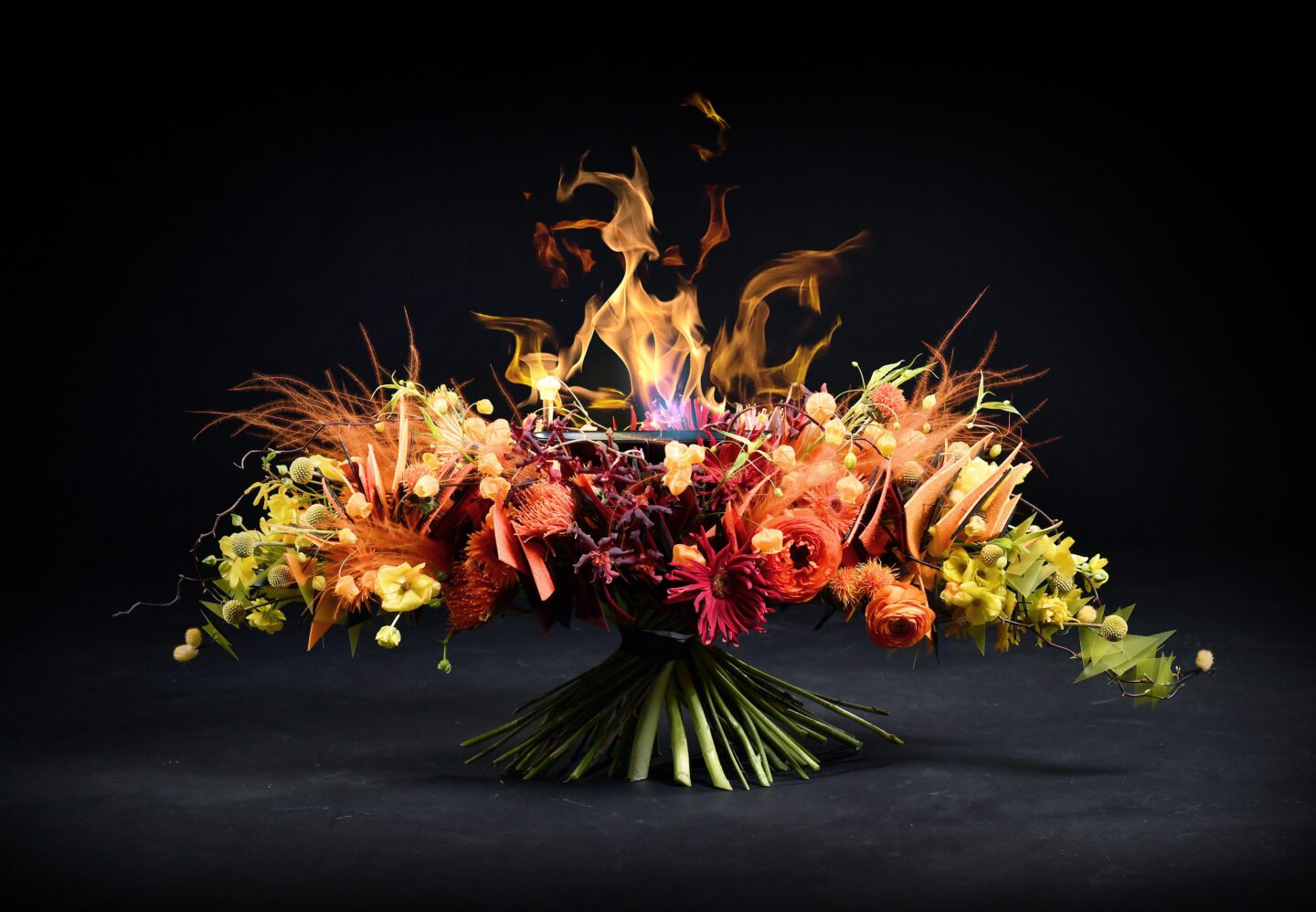 Vibrant floral arrangement with orange and yellow flowers, surrounded by flames against a black background.