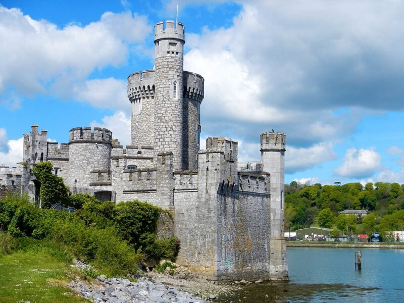 Blackrock Castle in Cork, featuring a stone structure with towers beside a river under a blue sky with clouds.
