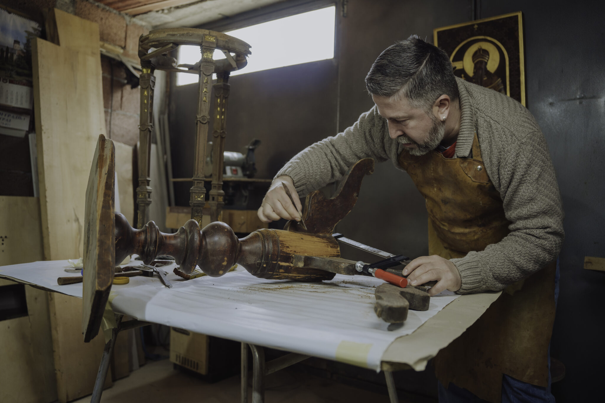 Craftsman repairing wooden furniture in a workshop, focused on a detailed section with tools nearby.