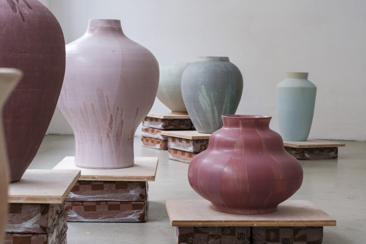 Ceramic vases in various pastel colors displayed on wooden platforms in an art studio.