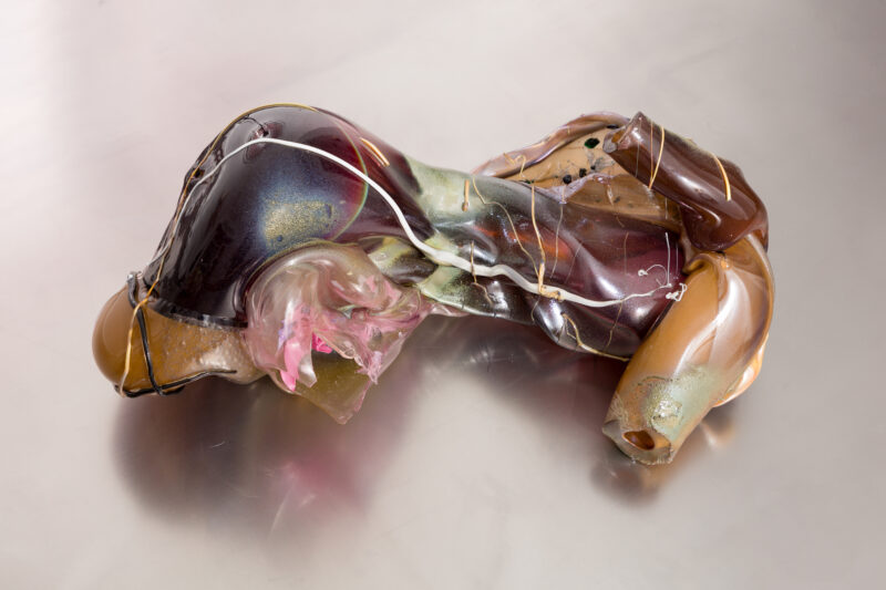 Abstract sculpture made of colorful, translucent materials, resembling organic forms, on a reflective surface.