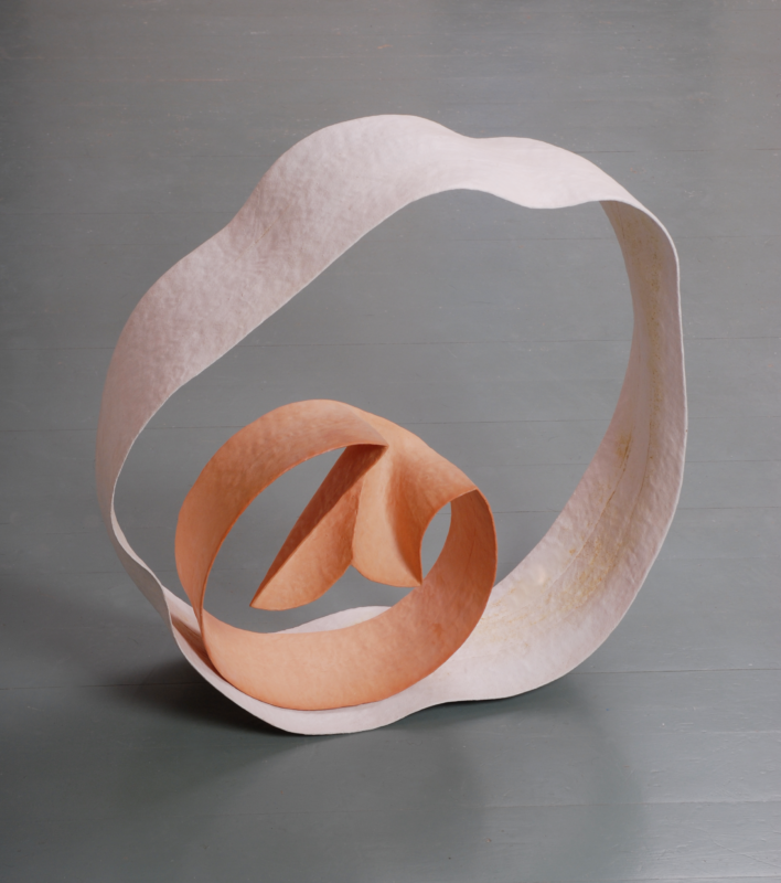 Abstract sculpture featuring intertwined loops of white and peach-colored material on a gray floor.