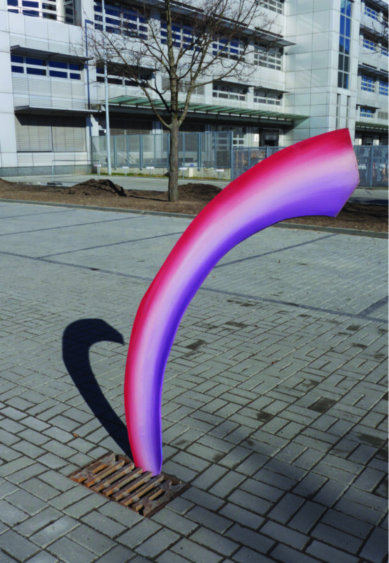Colorful curved sculpture in pink and purple, casting a shadow on a paved area near a building.
