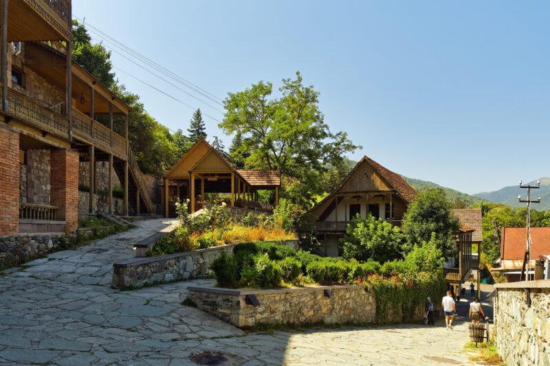 Scenic view of a stone pathway leading through a quaint village in Dilijan, Armenia, surrounded by greenery and wooden bui...