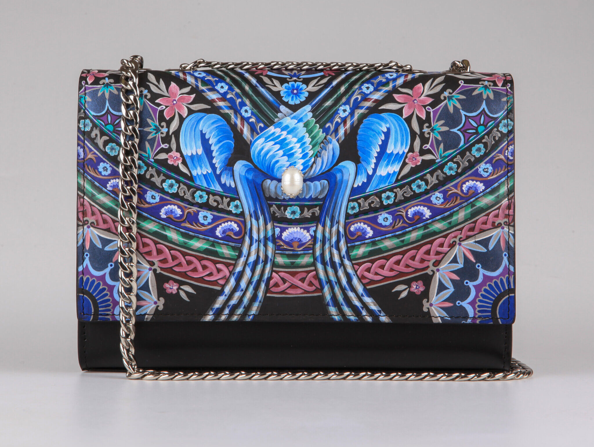 Colorful handbag featuring intricate floral and bird designs, with a chain strap and a pearl accent on the front.