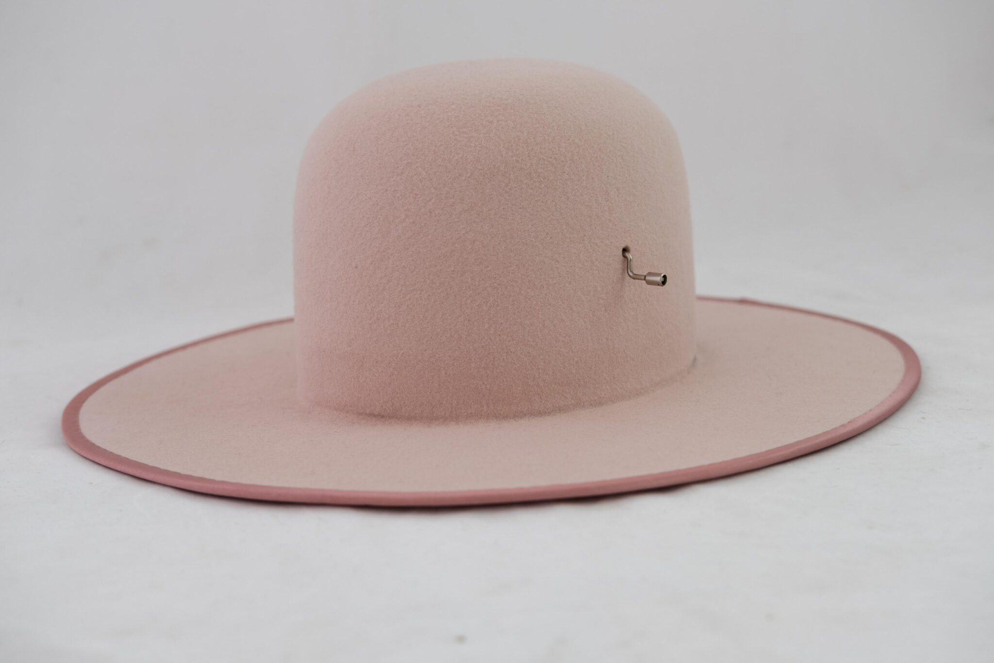 Pink felt hat with a wide brim and a small decorative pin, designed to incorporate a music box.