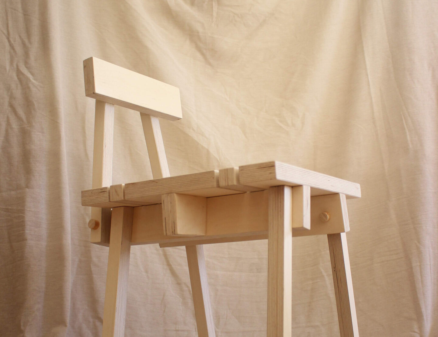 Minimalist wooden chair with a simple backrest, set against a neutral fabric backdrop.