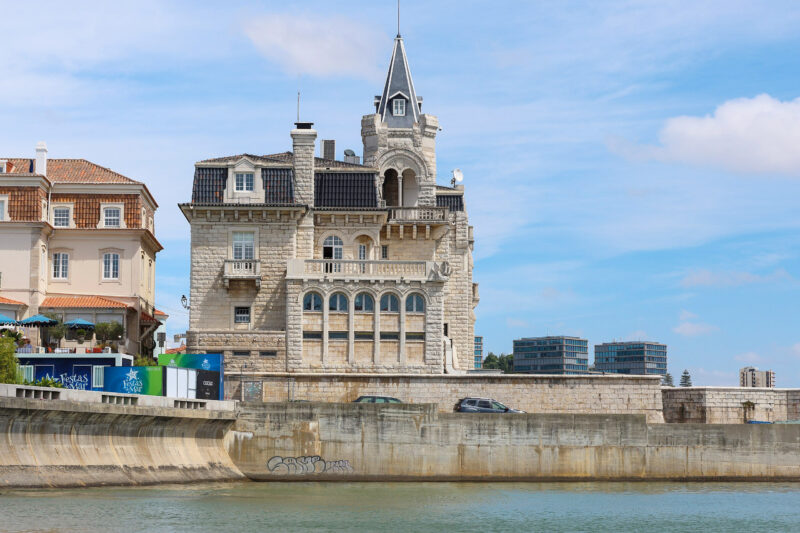 Historic building with ornate architecture along the shore in Cascais, Portugal, under a blue sky.
