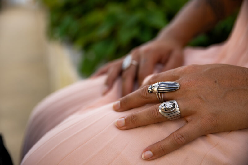 Close-up of a person's hands resting on a pink dress, showcasing multiple silver rings against a blurred green background.