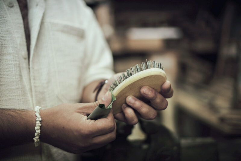 Hands holding a wooden brush with bristles, preparing it for use in a workshop setting.