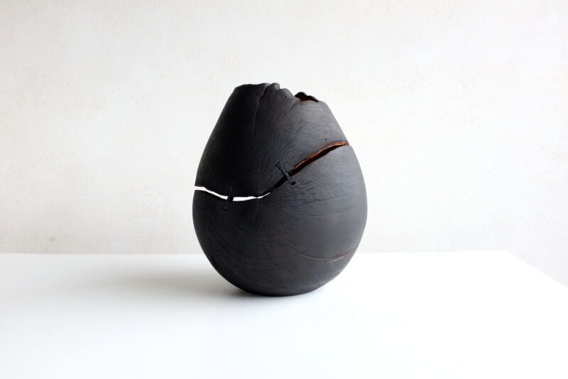 Black ceramic vase with a cracked surface, symbolizing rituals, on a white table against a light background.
