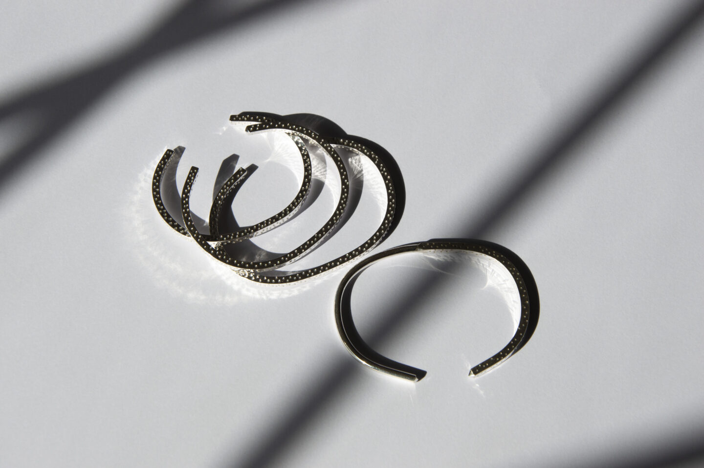 Minimalist bracelets with subtle textures displayed on a white surface, featuring soft shadows.