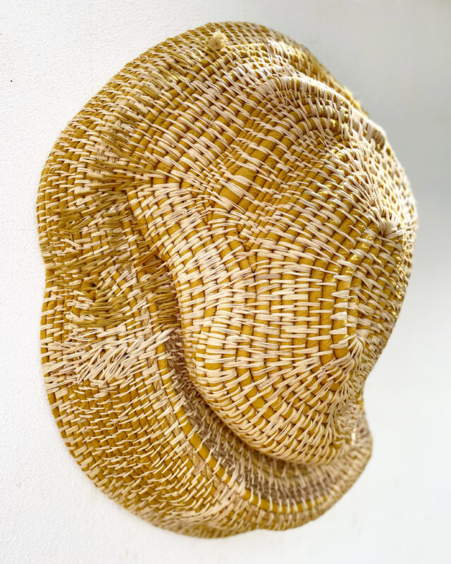 Woven yellow straw hat displayed against a white background, part of Maria Pratas' artwork "DUNAS.