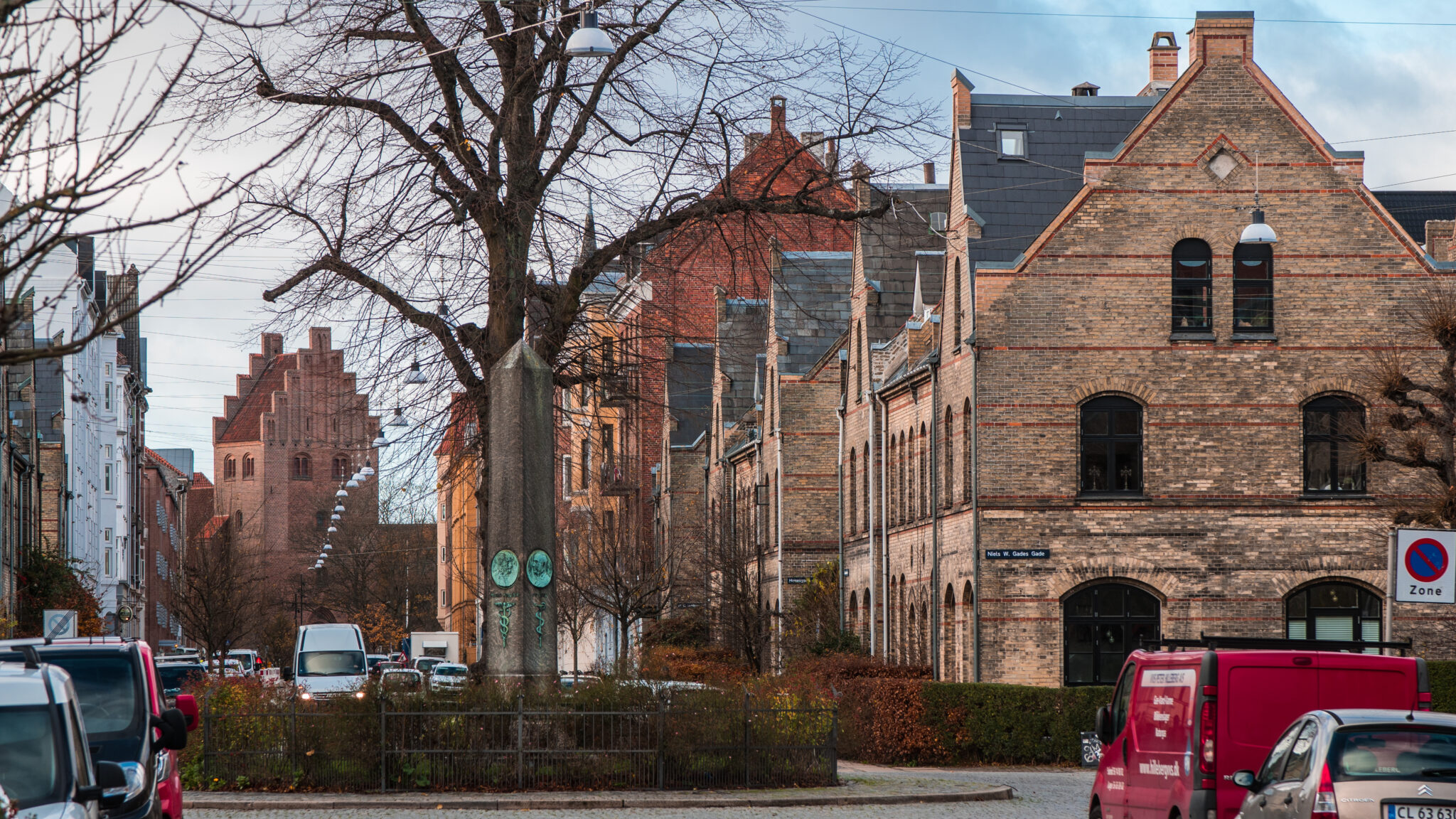 Copenhagen street scene featuring charming old buildings, trees, and parked cars.