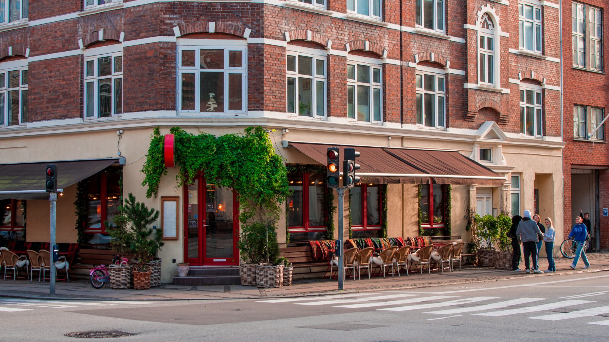 Copenhagen street corner featuring a cozy café with outdoor seating and pedestrians, surrounded by brick buildings.