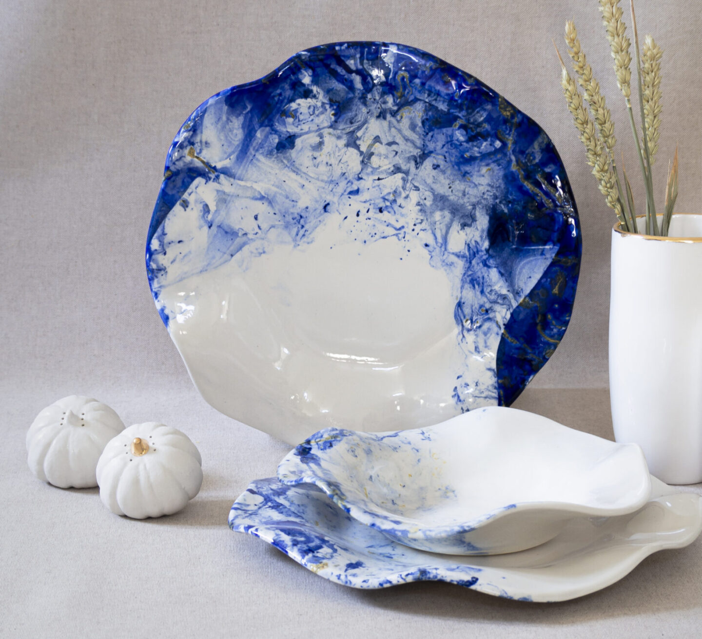 White ceramic plates with blue marbling, accompanied by small white pumpkins and a vase with dried grass.
