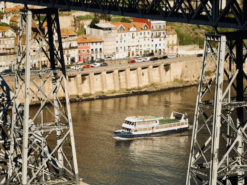 View of a river with a boat passing beneath a bridge, and colorful buildings lining the shore.