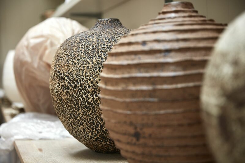 Textured ceramic vases in various shapes and finishes, showcasing nature's unpolished beauty in an artist's studio.