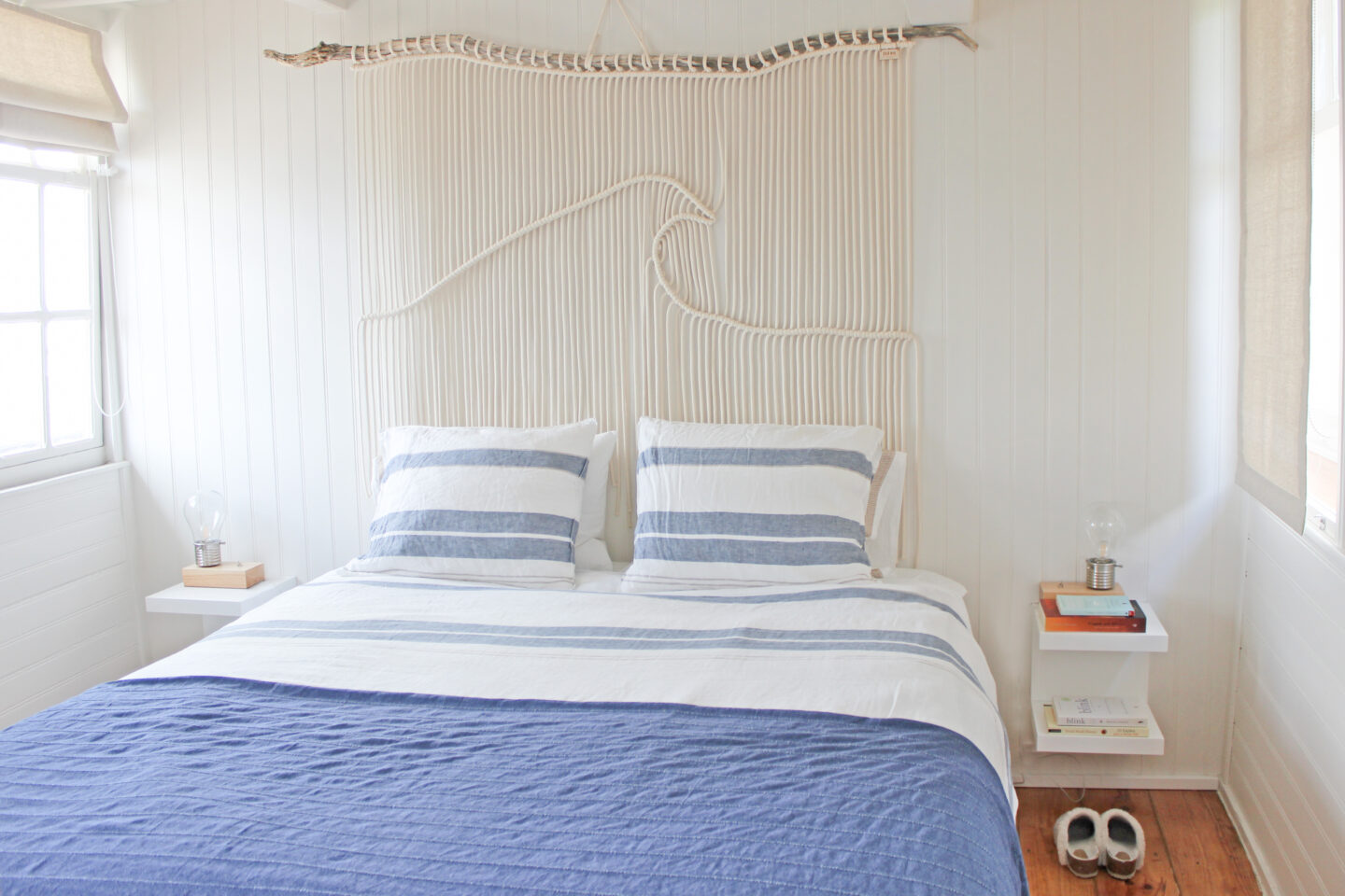 Cozy bedroom featuring a bed with blue and white striped bedding, a rope wave art piece, and natural light from a window.