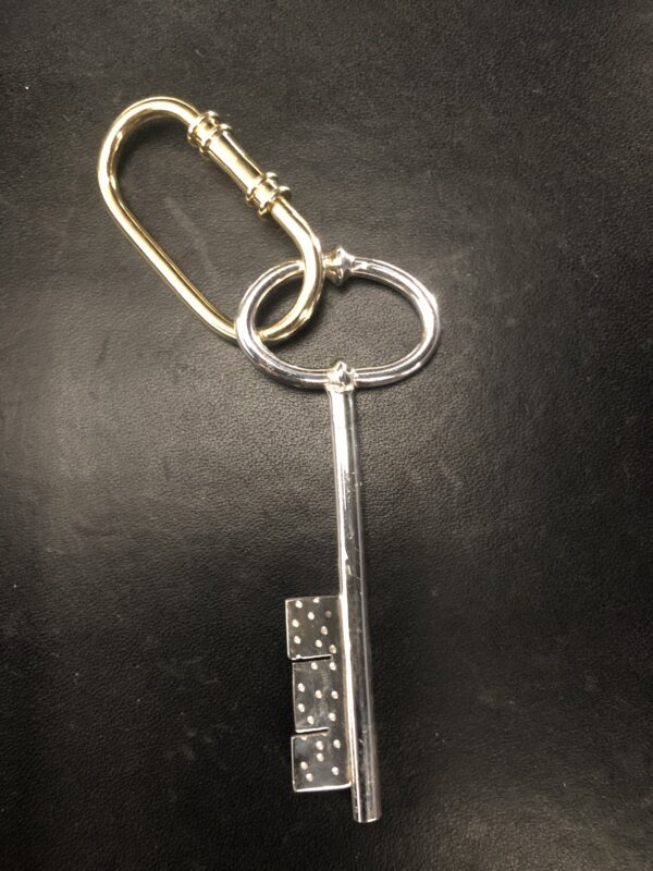 A large silver key with a decorative handle attached to a gold carabiner, set against a dark background.