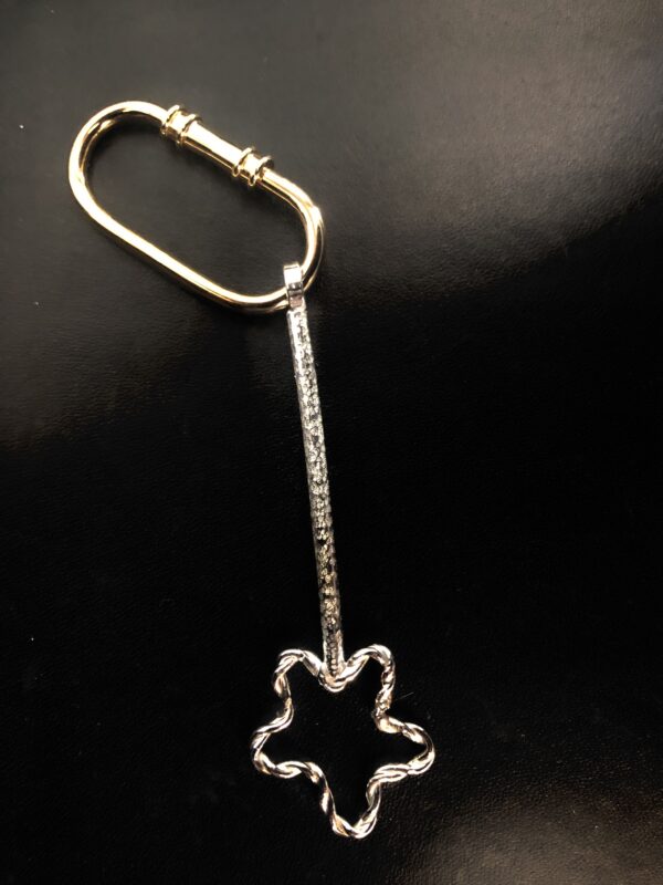 A silver key-shaped charm with a star outline, resembling a magic wand, on a black background.
