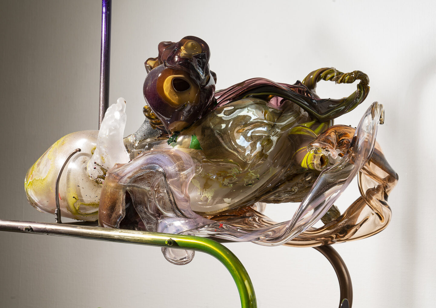Colorful glass sculpture with organic shapes, featuring intricate details and textures, displayed on a metallic stand.
