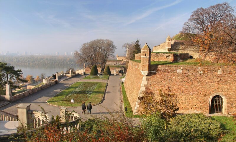 View of Kalemegdan Fortress in Belgrade, featuring stone walls, trees, and a pathway along the river.