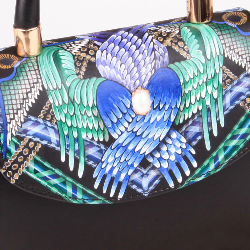 Colorful handbag featuring intricate wing designs in blue and green on a black background, with a pearl embellishment.