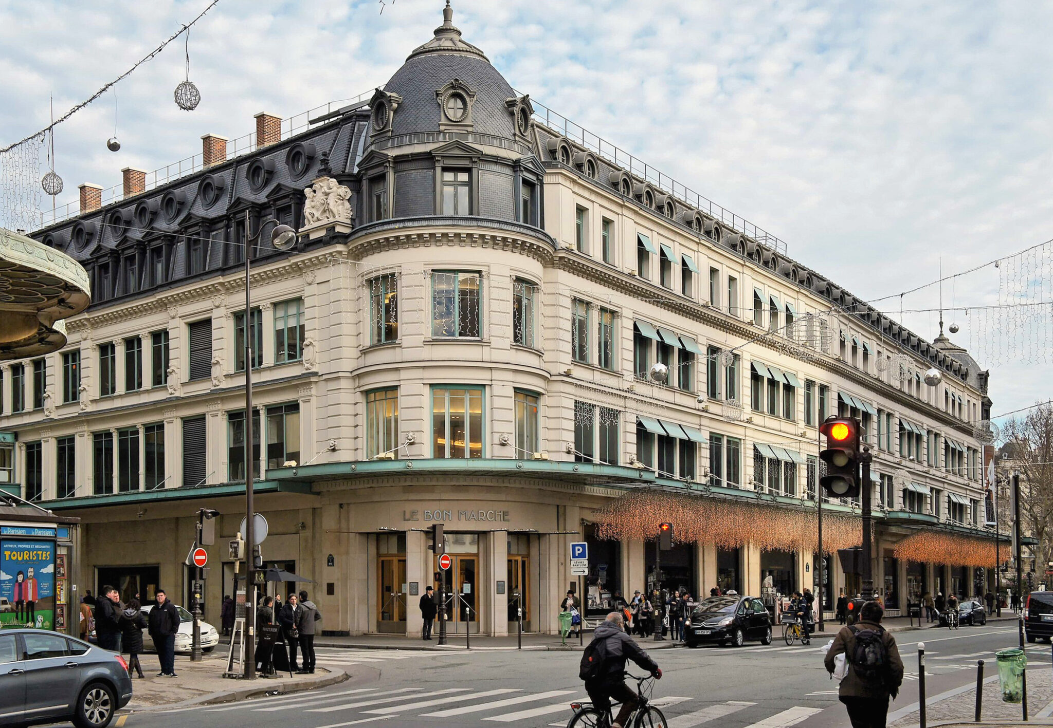 Le Bon Marché, the first department store, viewed from the street with pedestrians and cyclists nearby.