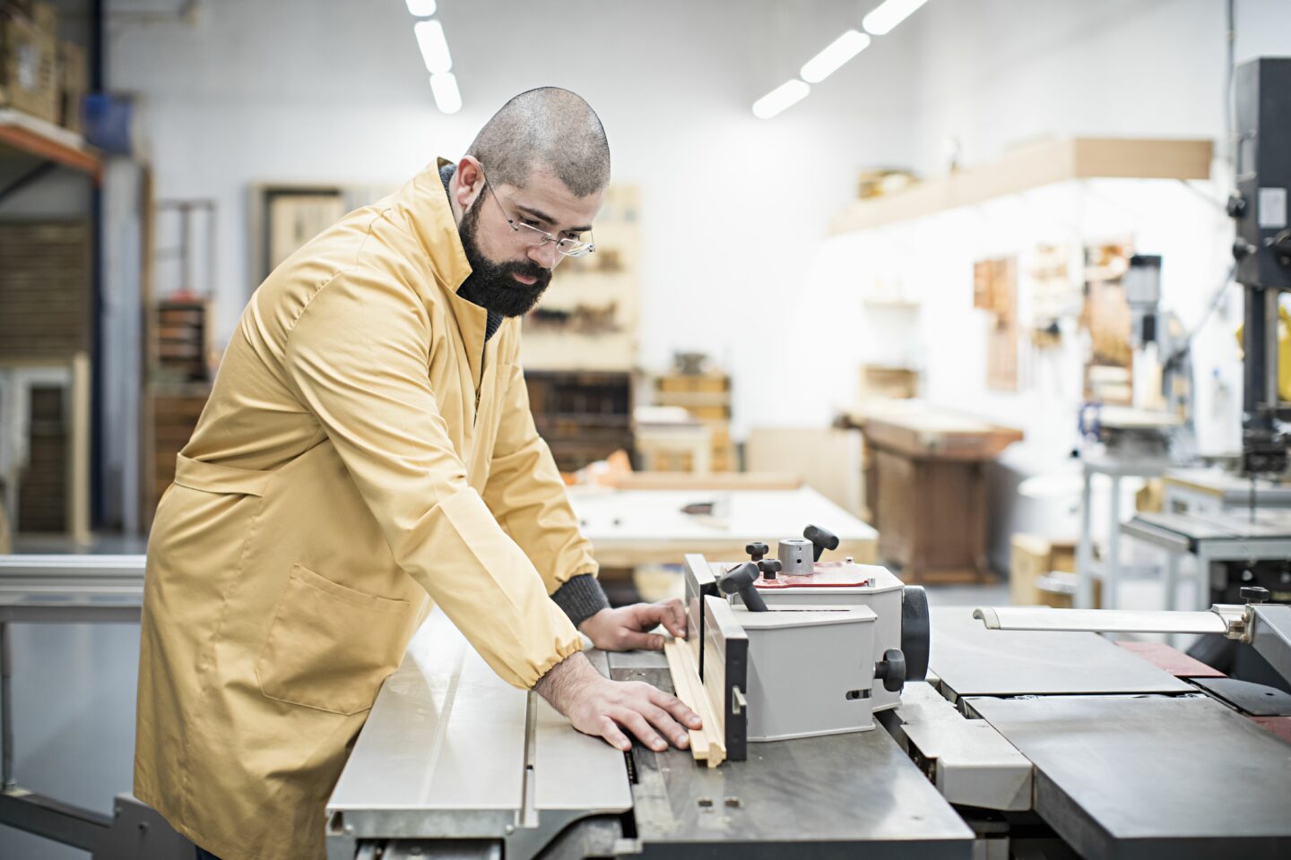 Tiago Pereira in a yellow coat, working at a woodworking machine in his studio.