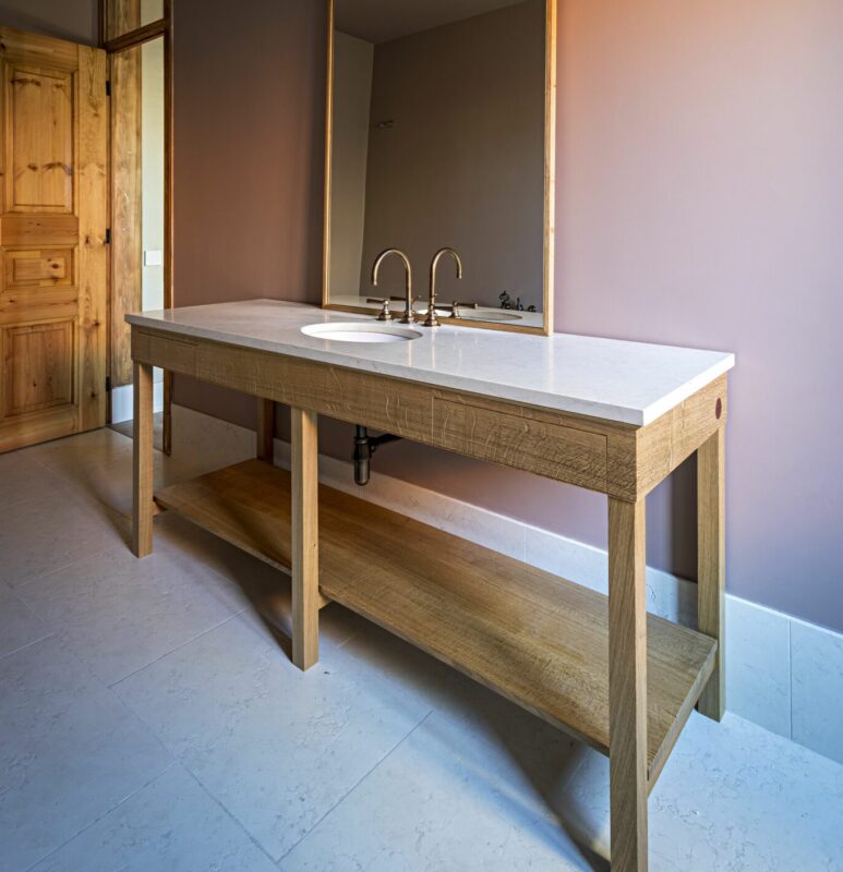 Bathroom vanity featuring a modern-rustic design, with a white countertop and wooden base against a muted wall.