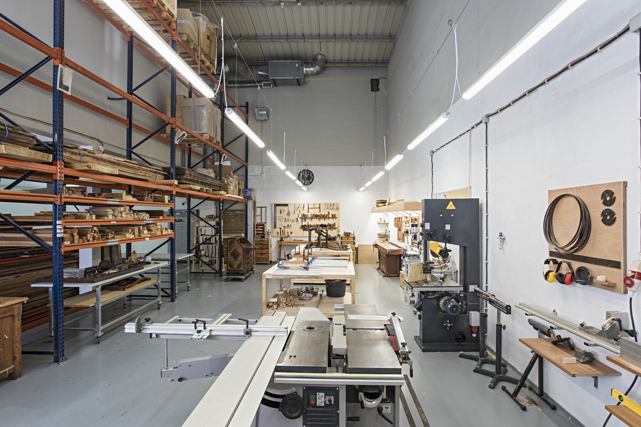 Wood workshop in a transformed warehouse, featuring shelves of wood, machinery, and worktables.