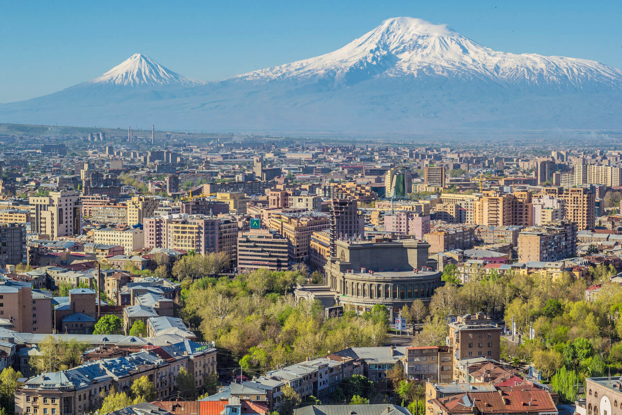 Mount Ararat towers over the Yerevan skyline, showcasing a mix of urban architecture and greenery.