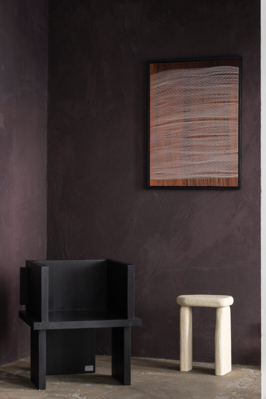 Textiles by Nathalie Van der Massen and furniture by Sizar & Sinar Alexis in a gallery setting with dark walls.