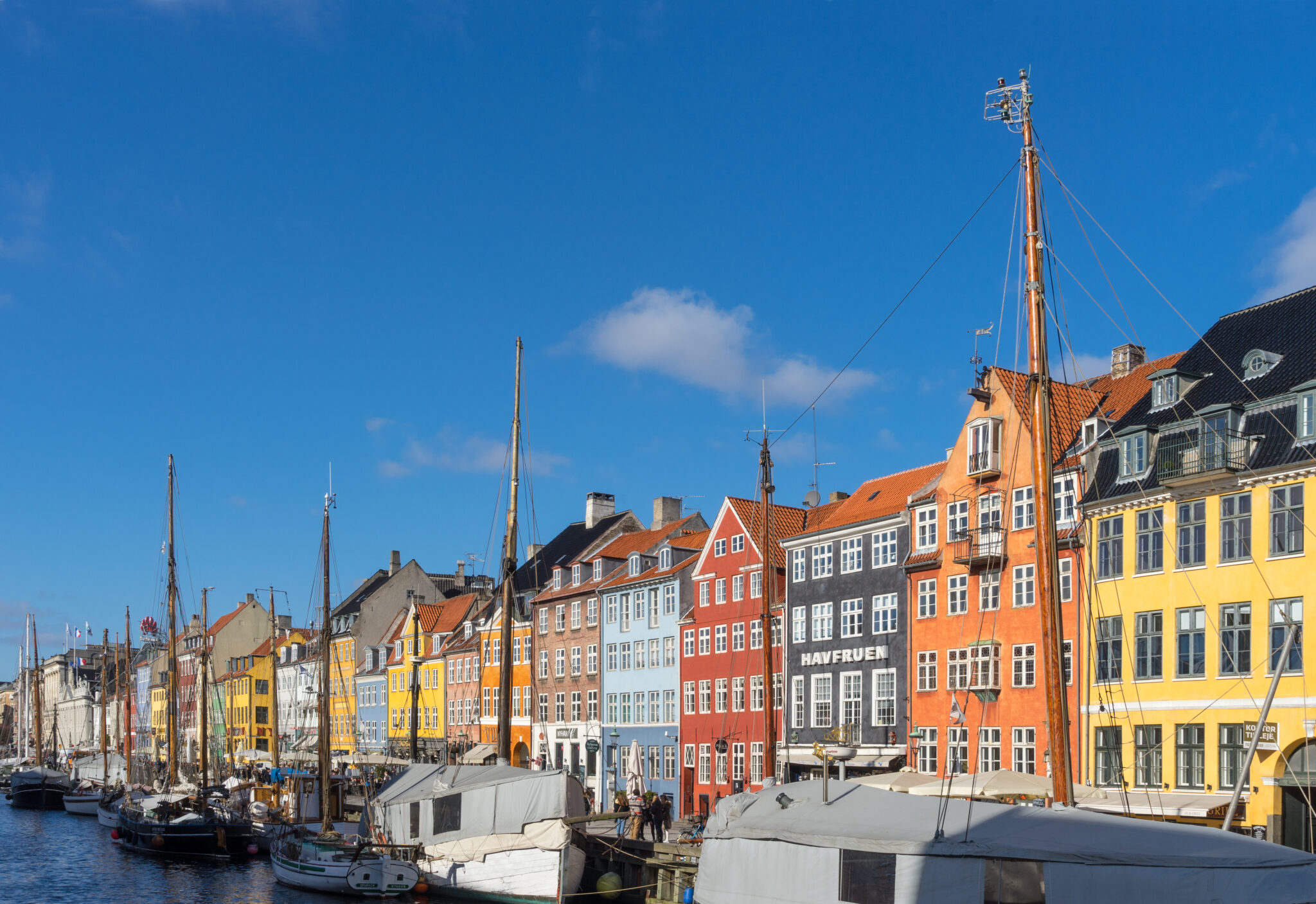 Colorful facades of historic buildings lining the waterfront in Nyhavn, Copenhagen, under a clear blue sky.