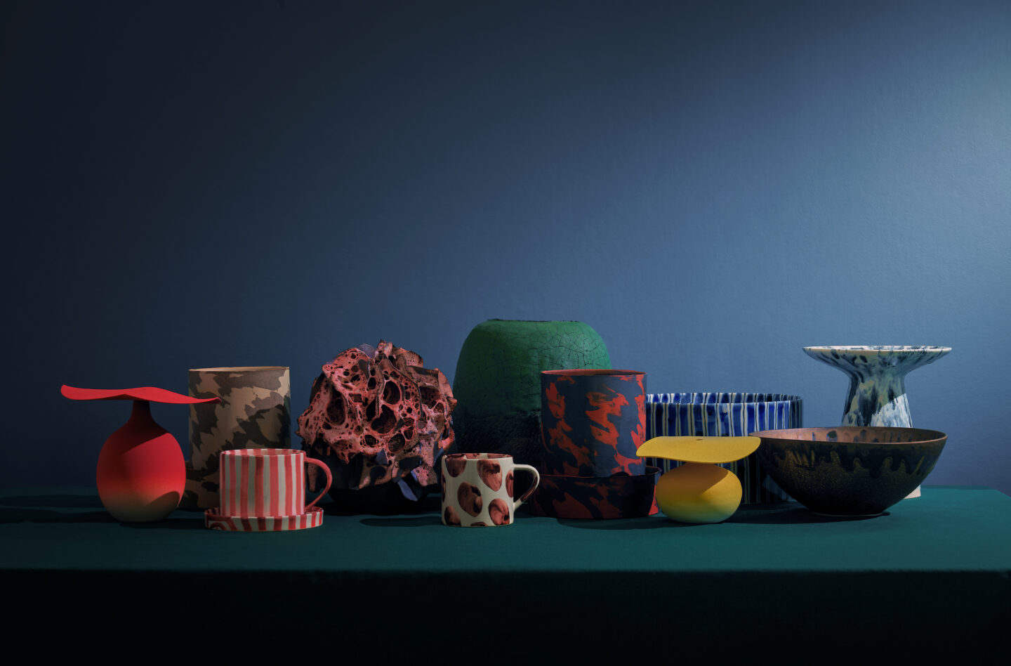 Colorful ceramics by Masayoshi Oya arranged on a green table against a dark blue background.