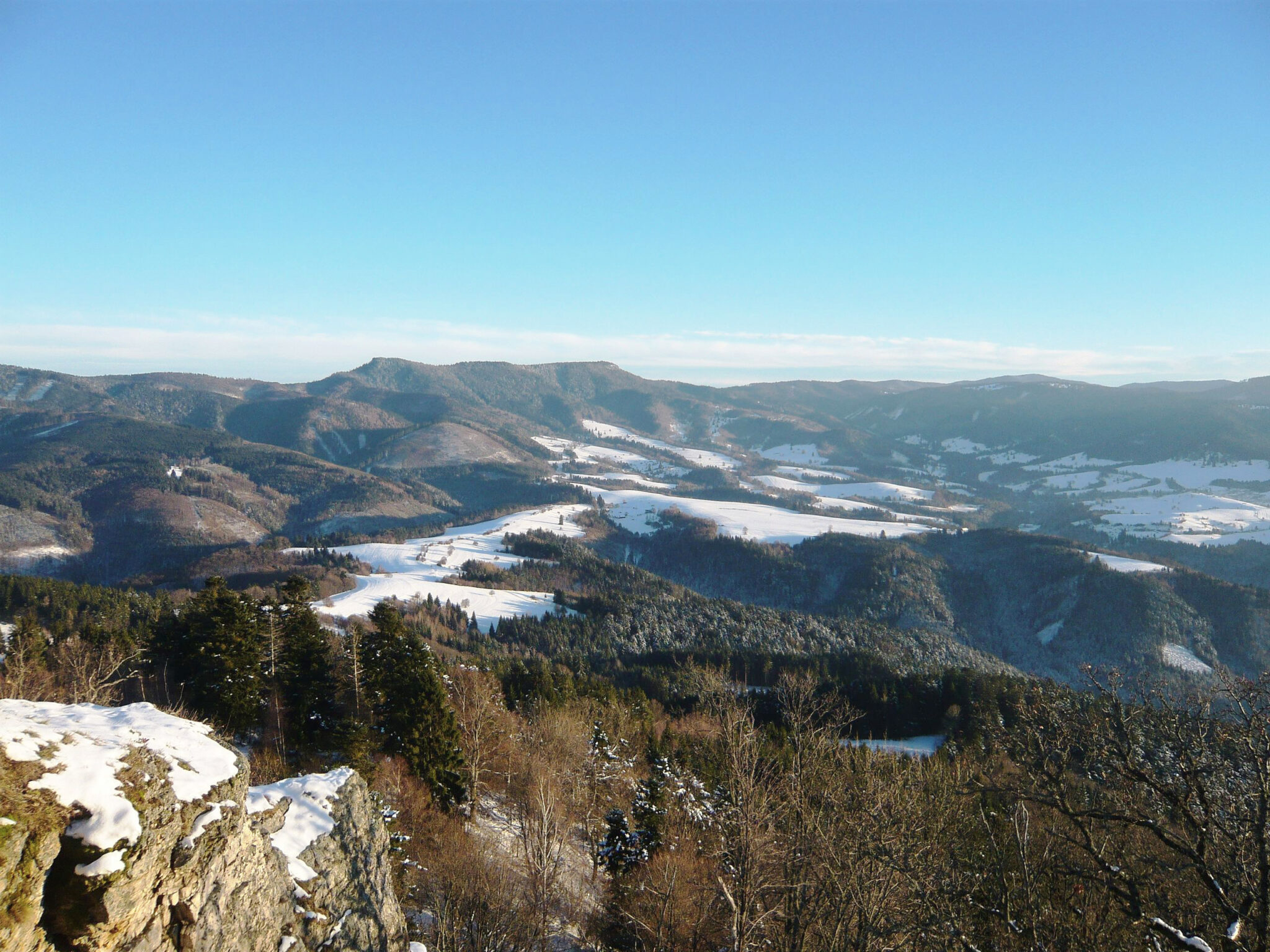 Winter landscape of Strelníky village at the foot of Poľany, featuring snow-covered hills and a clear blue sky.