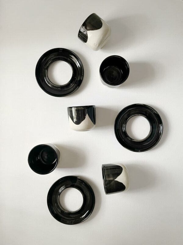 Black and white ceramic cups and saucers arranged artistically on a white background.