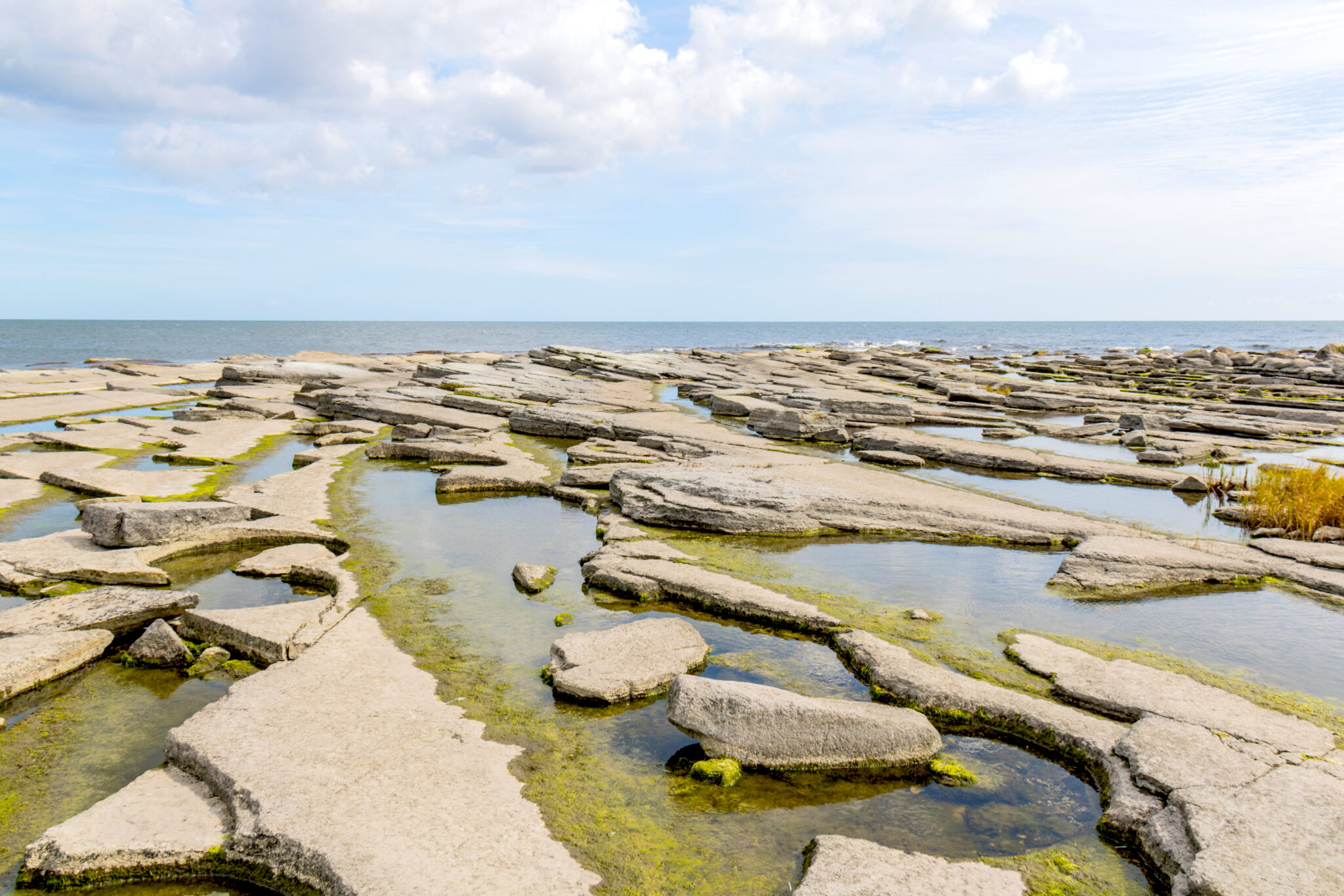 Rocky shoreline with flat stone formations and shallow pools, under a partly cloudy sky at Österlen.