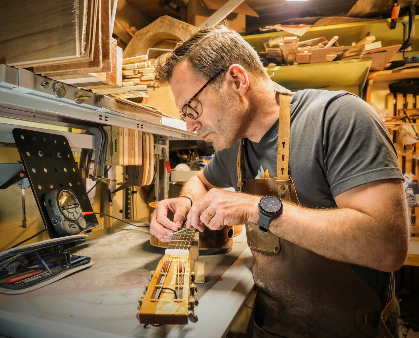 Craftsman Janne Koskela meticulously works on a guitar neck in a well-equipped workshop, focusing on precision and detail.