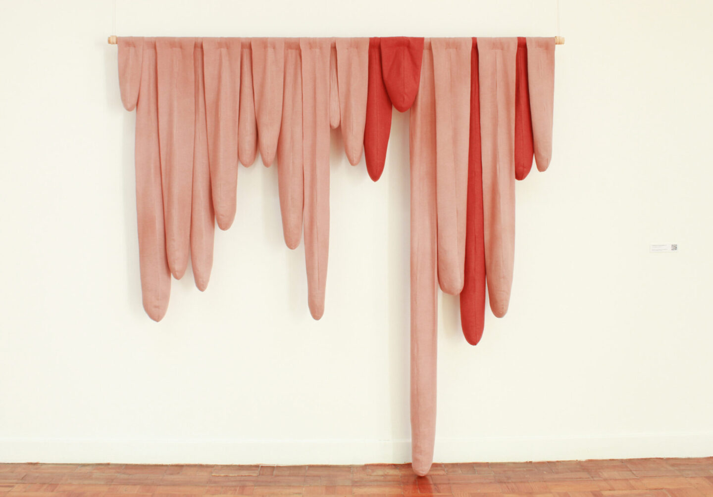 Textile sculpture resembling colorful melting stalactites, featuring elongated forms in shades of red and pink.