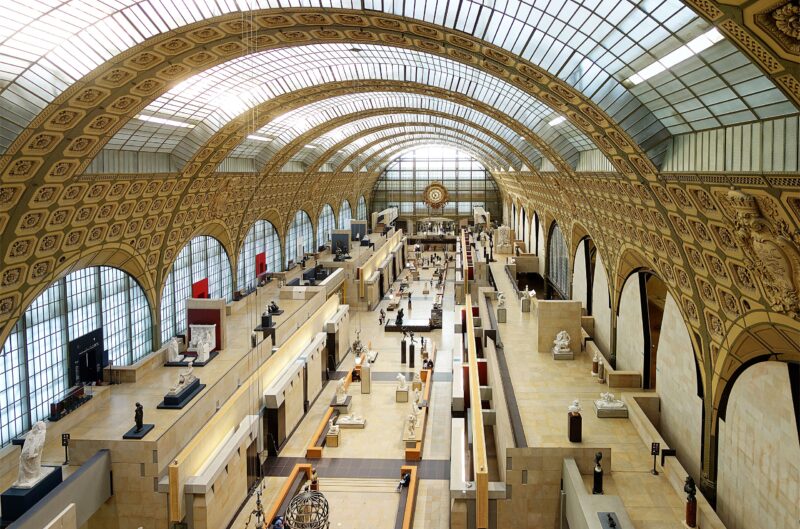 Grand hall of the Musée d'Orsay with high arched ceiling and numerous sculptures displayed throughout.