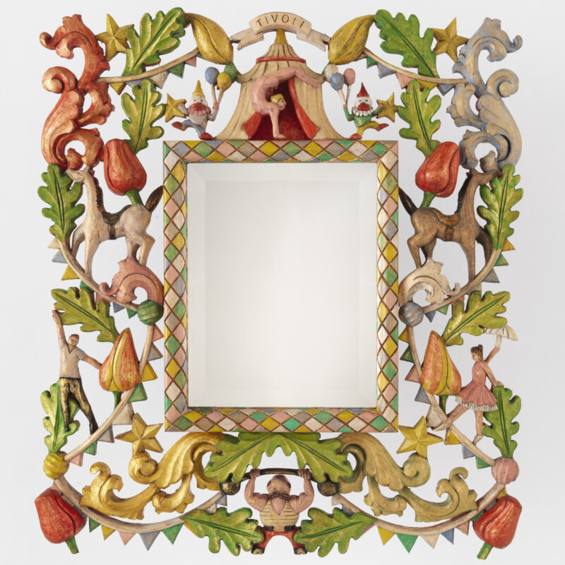 Colorful, ornate mirror frame with intricate carvings of animals, flowers, and circus figures, featuring a blank central m...