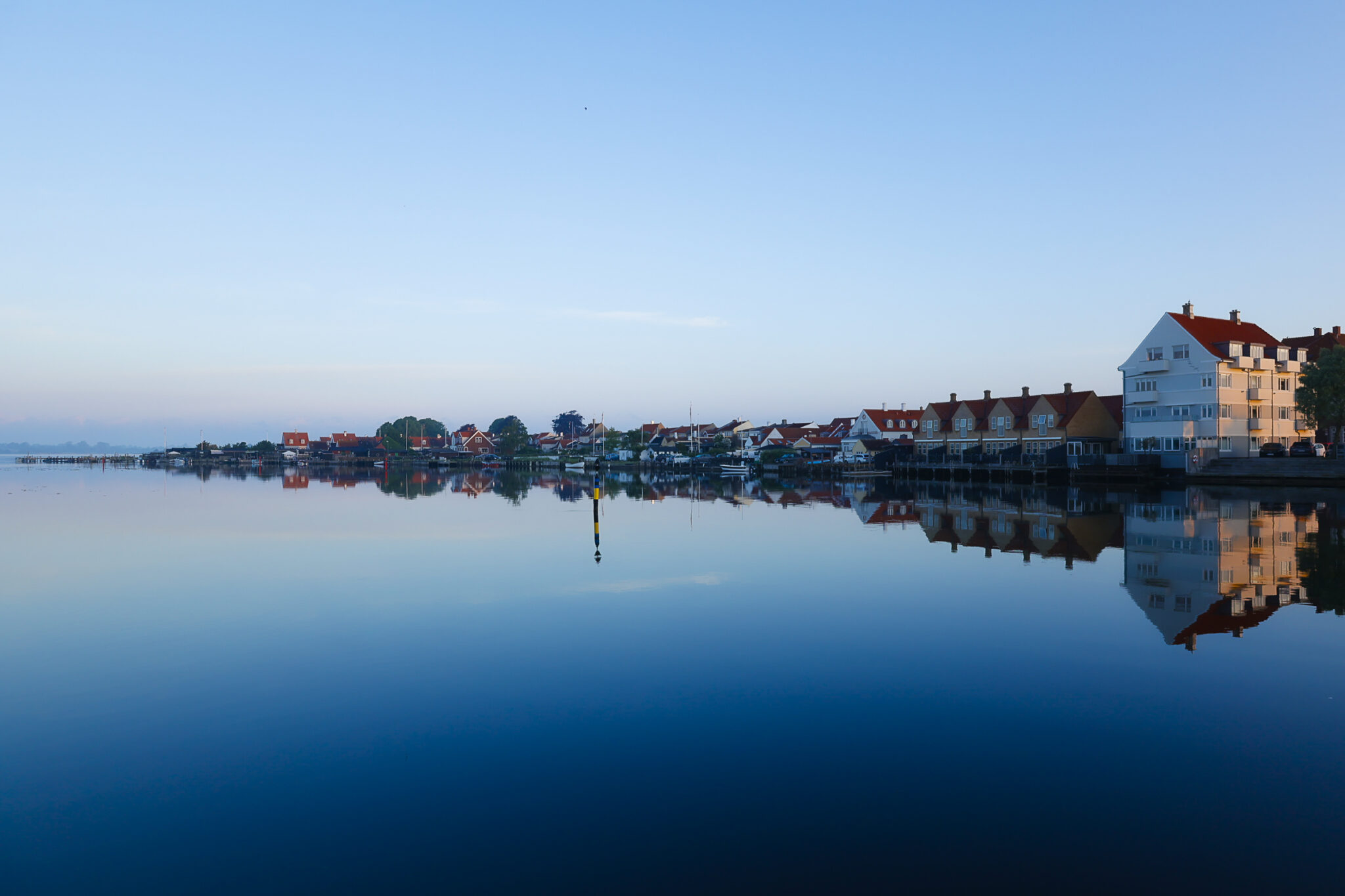 Calm waters reflect colorful buildings in Kerteminde, blurring the line between town and tide at dawn.
