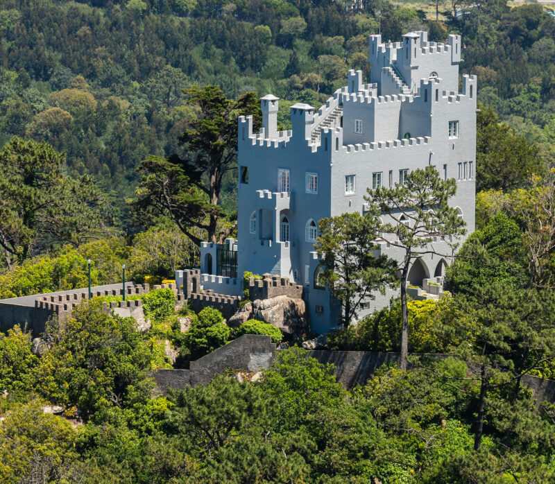 National Palace of Sintra surrounded by lush greenery, showcasing its unique architecture against a blue sky.